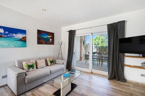 Ein modernes Wohnzimmer mit einer Couch, einem Glastisch, einem Flachbildfernseher und einer Schiebetür zu einem Außenbereich.