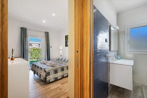 Ein modernes Schlafzimmer mit Bett, ein Badezimmer mit Waschbecken und Blick auf einen Garten.