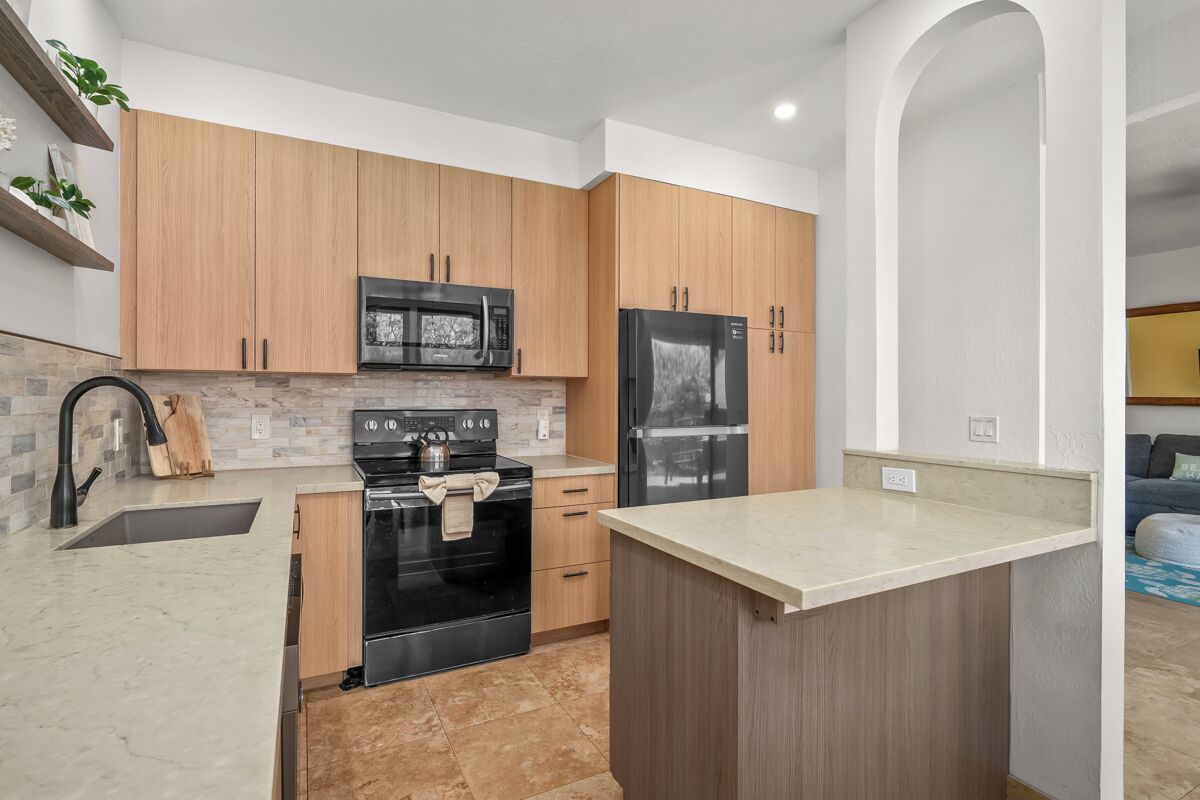 A modern kitchen with wooden cabinets, a black stove, a microwave, and a refrigerator.