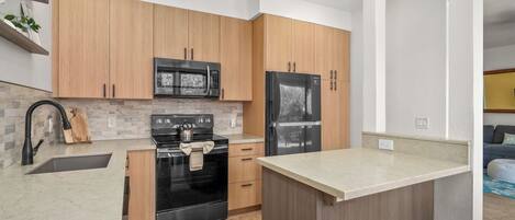 A modern kitchen with wooden cabinets, a black stove, a microwave, and a refrigerator.