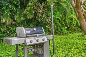 Ein Weber-Gasgrill mit vier Brennern, einer Seitablagefläche und einem Starter für den Grillanzünder in einem Garten.