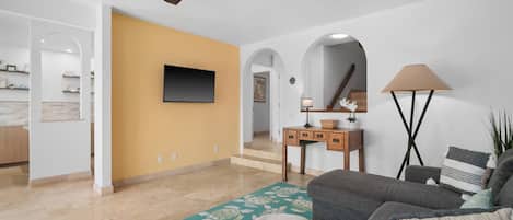Una sala de estar con un sofá, una televisión, una lámpara y un ventilador de techo.