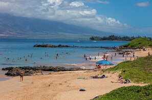 A beach with people swimming and sunbathing, a rocky outcrop, and a distant mountain range. - Ground Floor Wailea Condo with Private Lanai Near Beaches (Kihei)
