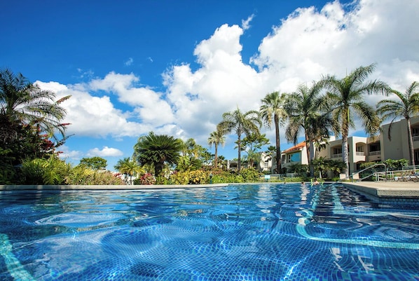 A clear blue pool surrounded by palm trees and a building with balconies. - Ground Floor Wailea Condo with Private Lanai Near Beaches (Kihei)