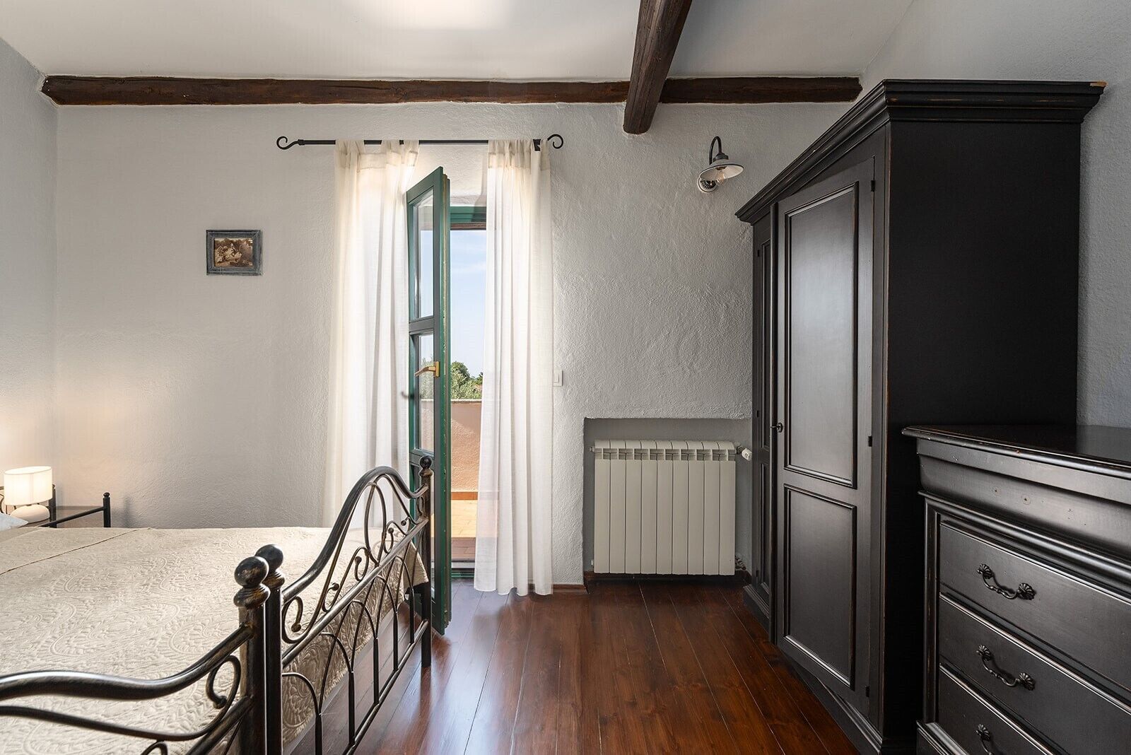 Une chambre à coucher avec un lit, un radiateur, une armoire et une fenêtre avec des rideaux.