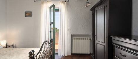 Une chambre à coucher avec un lit, un radiateur, une armoire et une fenêtre avec des rideaux.
