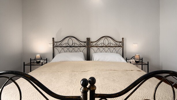 Una cama doble con estructura metálica, dos mesitas de noche con lámparas y una lámpara de pared.