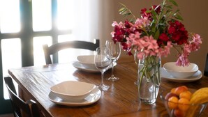 Una mesa de madera con platos blancos, copas de vino transparentes y un jarrón con flores rosadas.