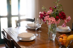 Ein Holztisch mit weißen Tellern, klaren Weingläsern und einer Vase mit rosa Blumen.