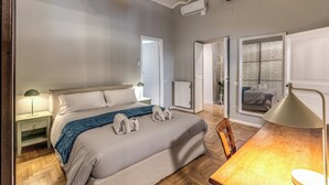 Ein Schlafzimmer mit einem Bett, Nachttischen, einer Lampe und Blick auf einen anderen Raum.
