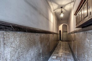 Un lungo corridoio rivestito in marmo, con una scala, un lampadario e armadi in legno.