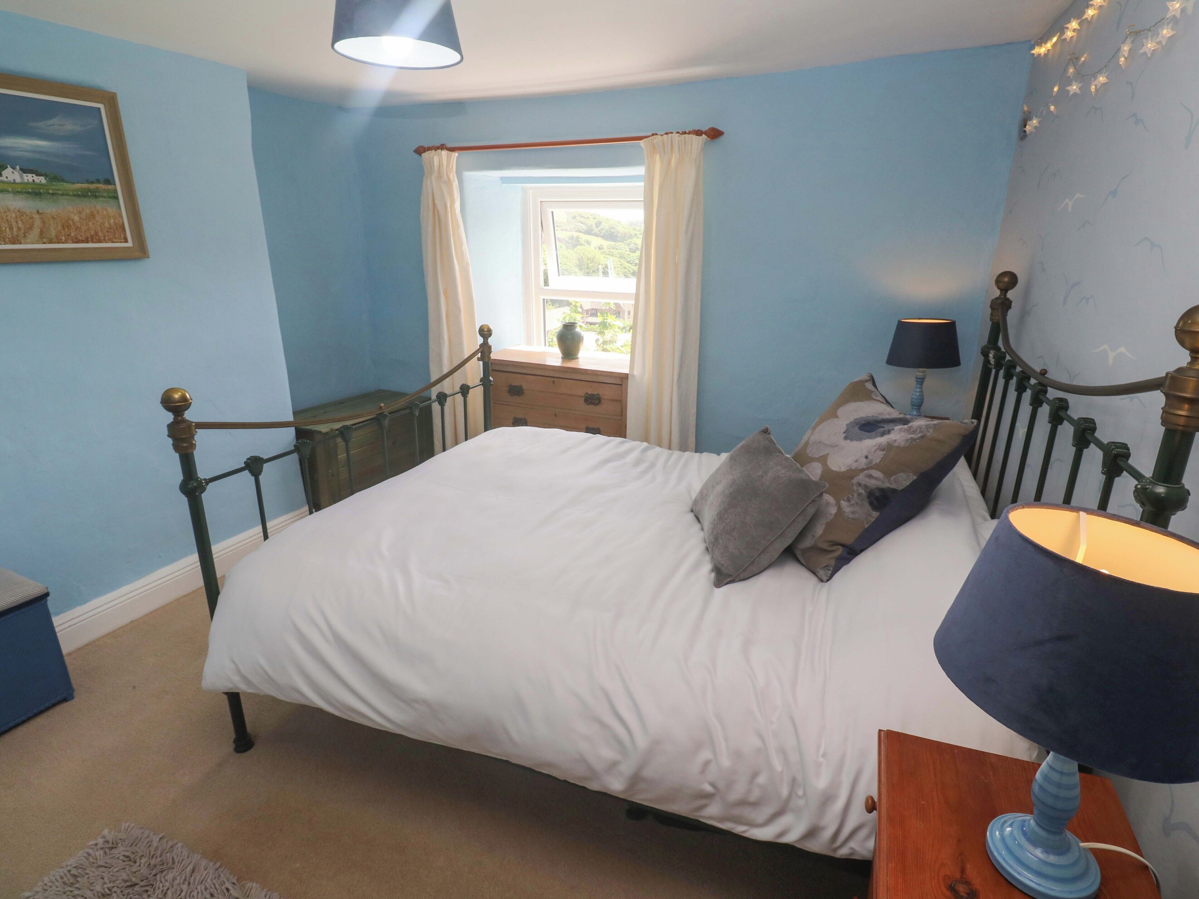 Une chambre à coucher avec un lit, une table de chevet, une lampe, une fenêtre avec des rideaux et un tableau au mur.