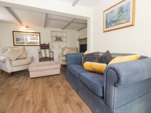A living room with a blue sofa, beige armchair, and ottoman, wooden flooring, and a framed painting on the wall. - Greenways (Perranporth)