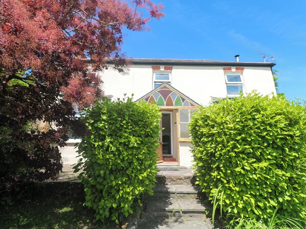 A building with a white exterior, a green door, and a window with a decorative frame. - Greenways (Perranporth)