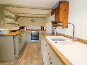 A compact kitchen with a microwave, oven, sink, and wooden cabinets. - Greenways (Perranporth)