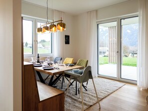 Ein Essbereich mit Holztisch, Stühlen und Blick auf eine grüne Landschaft durch große Fenster.