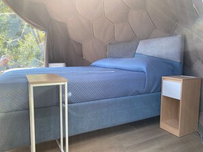 A modern bedroom with a geometric headboard, a bed with blue bedding, a wooden nightstand, and a small table. - Vrbo Property (Marciano)