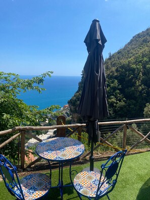 A terrace with a table and chairs, a view of the sea, and a forested hillside. - Vrbo Property (Marciano)