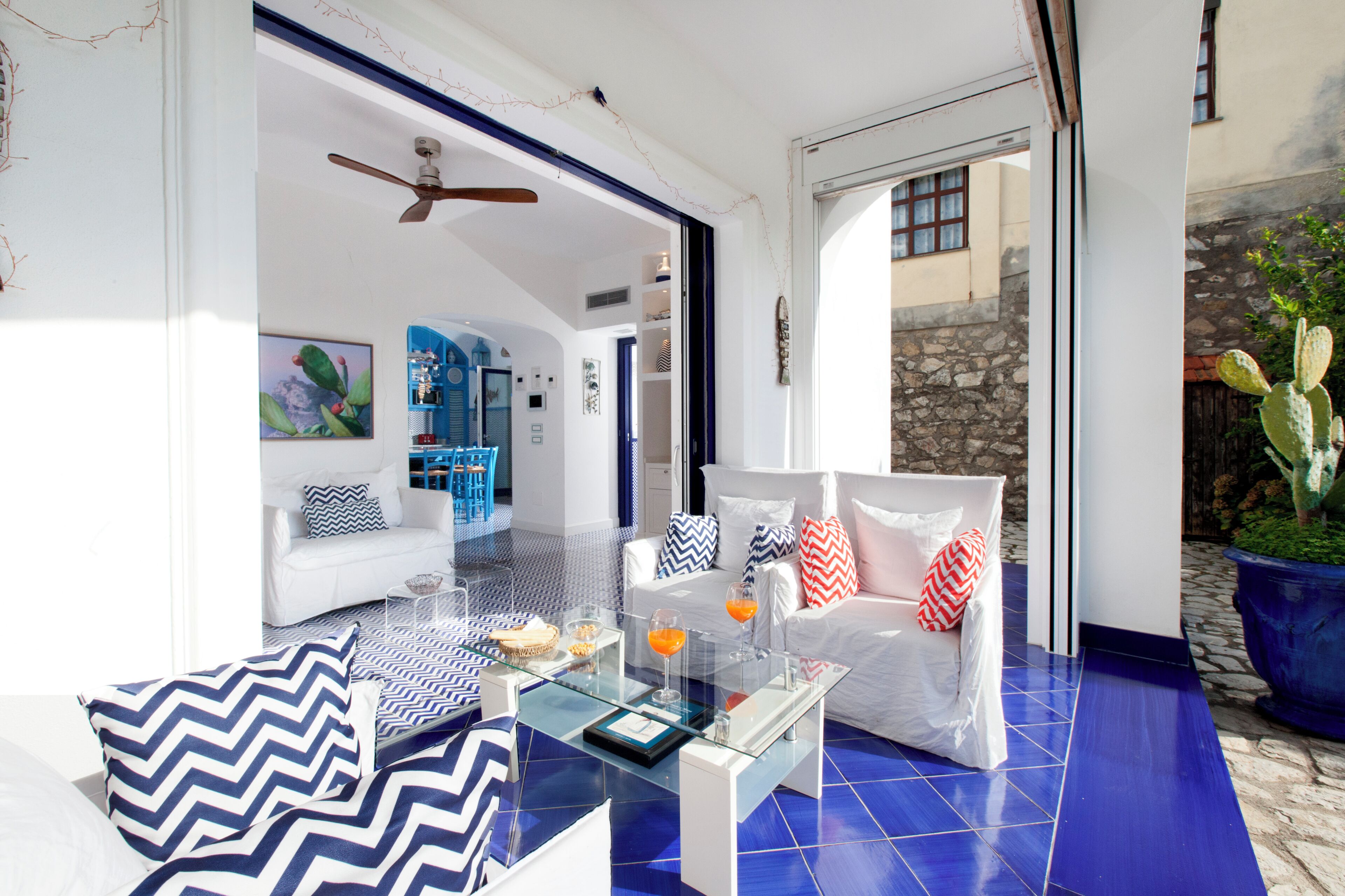 Un salon moderne avec une table basse en verre, des canapés blancs et un sol carrelé de couleur bleue.