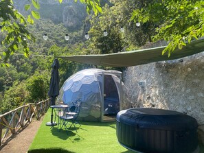 A dome-shaped tent with a table and chairs, a hot tub, and a view of a mountainous landscape. - Vrbo Property (Marciano)