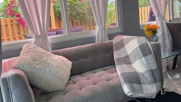 Un divano grigio con un cuscino soffice e una coperta a quadri, un tavolino in vetro e un vaso con fiori.