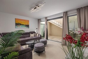 Ein modernes Wohnzimmer mit Sofa, Hocker und Couchtisch, einem Bild an der Wand und einer Treppe, die zu einem Balkon führt.