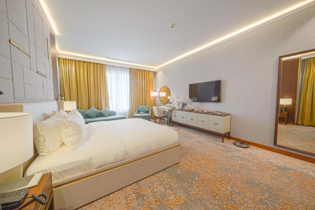 Una habitación de hotel con una cama grande, un escritorio, una silla, un aparador, un televisor y un espejo.