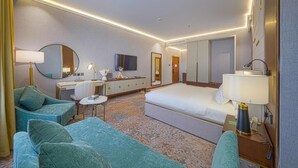 Una habitación de hotel con una cama, dos sillones, un escritorio, un televisor y un espejo.