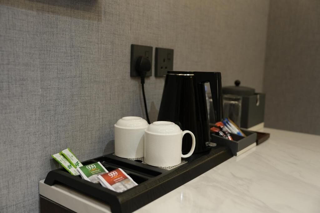Una estación de café con dos tazas blancas, una cafetera y sobres de café.