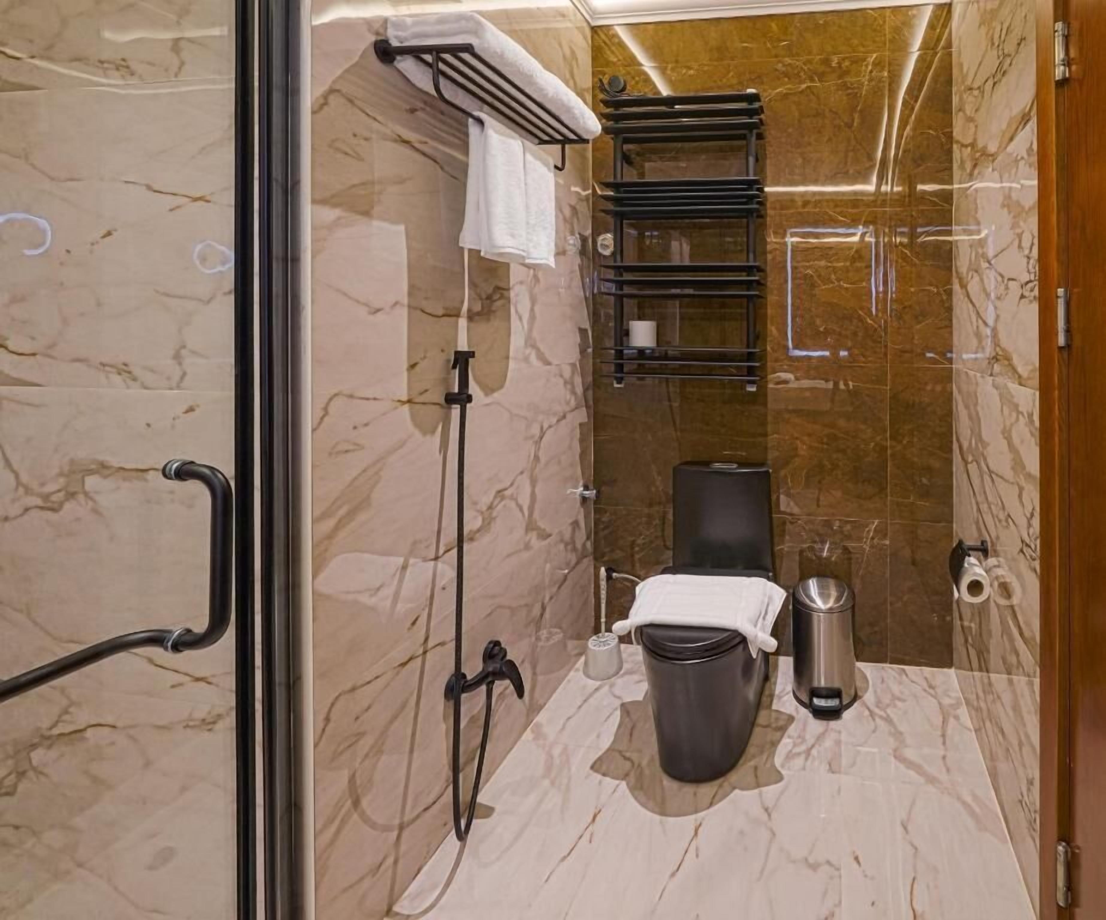 Casa de banho com chão de mármore, sanita, um cesto de lixo, um porta-toalhas e área de chuveiro.