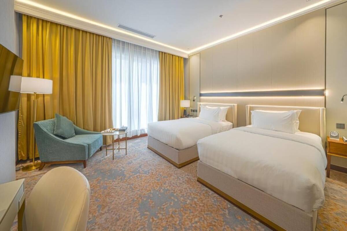 Hotellihuone, jossa on kaksi sänkyä, sohva, työpöytä ja lamppu.