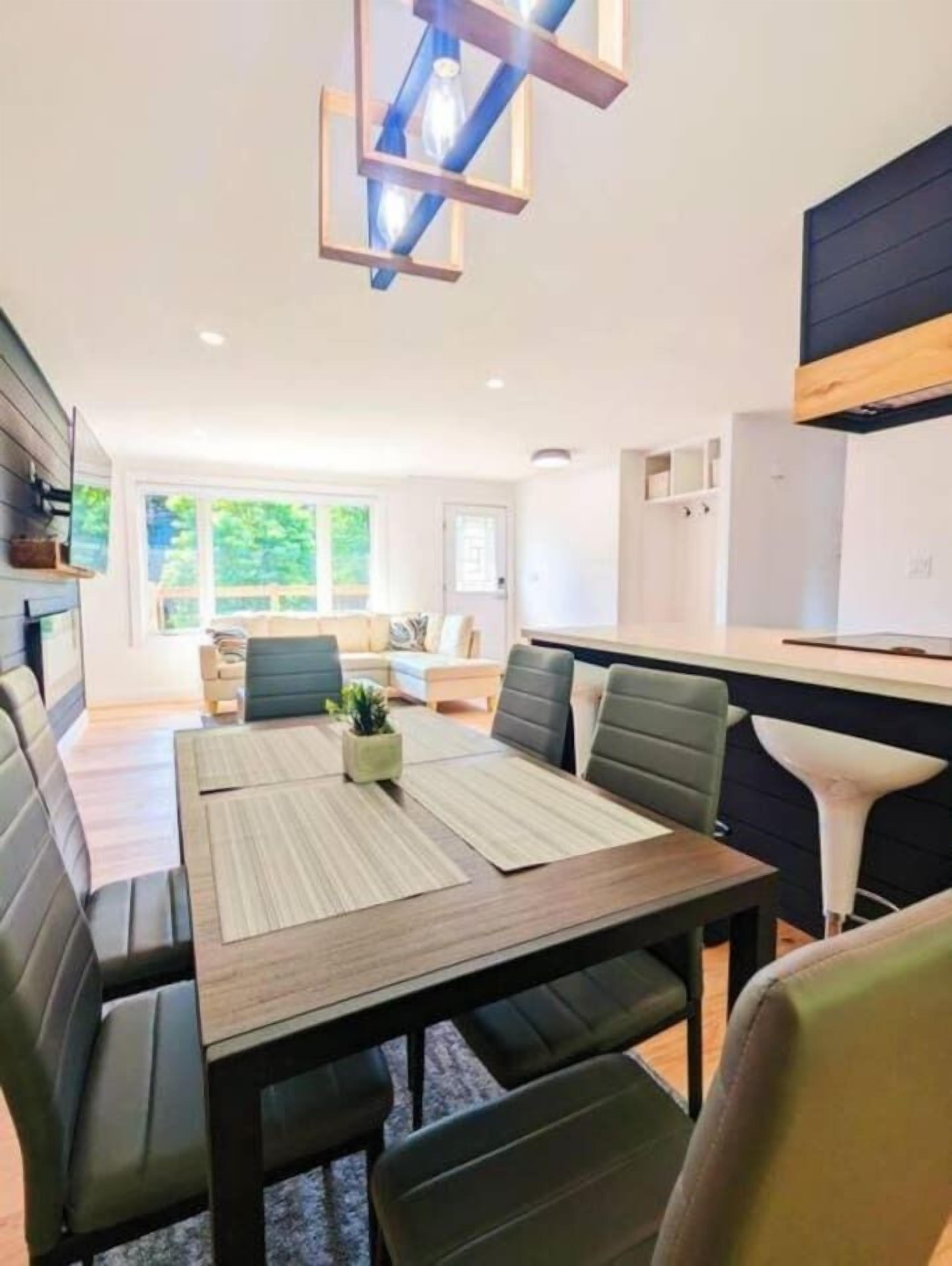 A modern dining area with a wooden table and cushioned seating, a pendant light, and a view of the outdoors.. Kingston Lodge: Comfy & Cozy w/ Natural Scenery