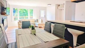 Uma sala de jantar moderna com mesa de madeira e assentos acolchoados, uma luminária pendente e vista para o exterior.