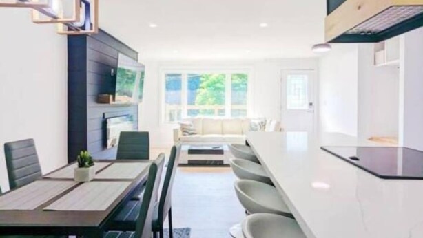 Uma cozinha moderna com bancada branca, sala de jantar com mesa e cadeiras, e vista para o exterior.