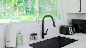 Uma cozinha moderna com uma janela grande, uma pia preta, uma torradeira e um lustre.