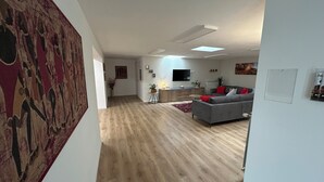 Amplia sala de estar con un sofá gris, cojines rojos, un televisor de pantalla plana y un cuadro abstracto grande en la pared.