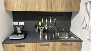 Una cocina con armarios de madera, cafetera, fregadero y utensilios colgados en la pared.