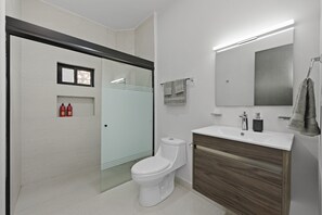 A modern bathroom with a toilet, a sink, a mirror, and a shower area. - Loft Moderno con 2 Queen Beds Zona Tec  loft 17 (Monterrey)