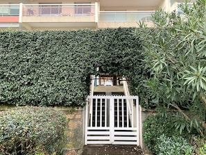 A gated entrance with a white gate, surrounded by dense green foliage and a building in the background. - New O'Bassin Apartment with Sea View, Private Terrace, and Wi-Fi (Arcachon)