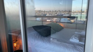 Et hotelværelse med en seng, puder, et natbord og udsigt til en havn med både.