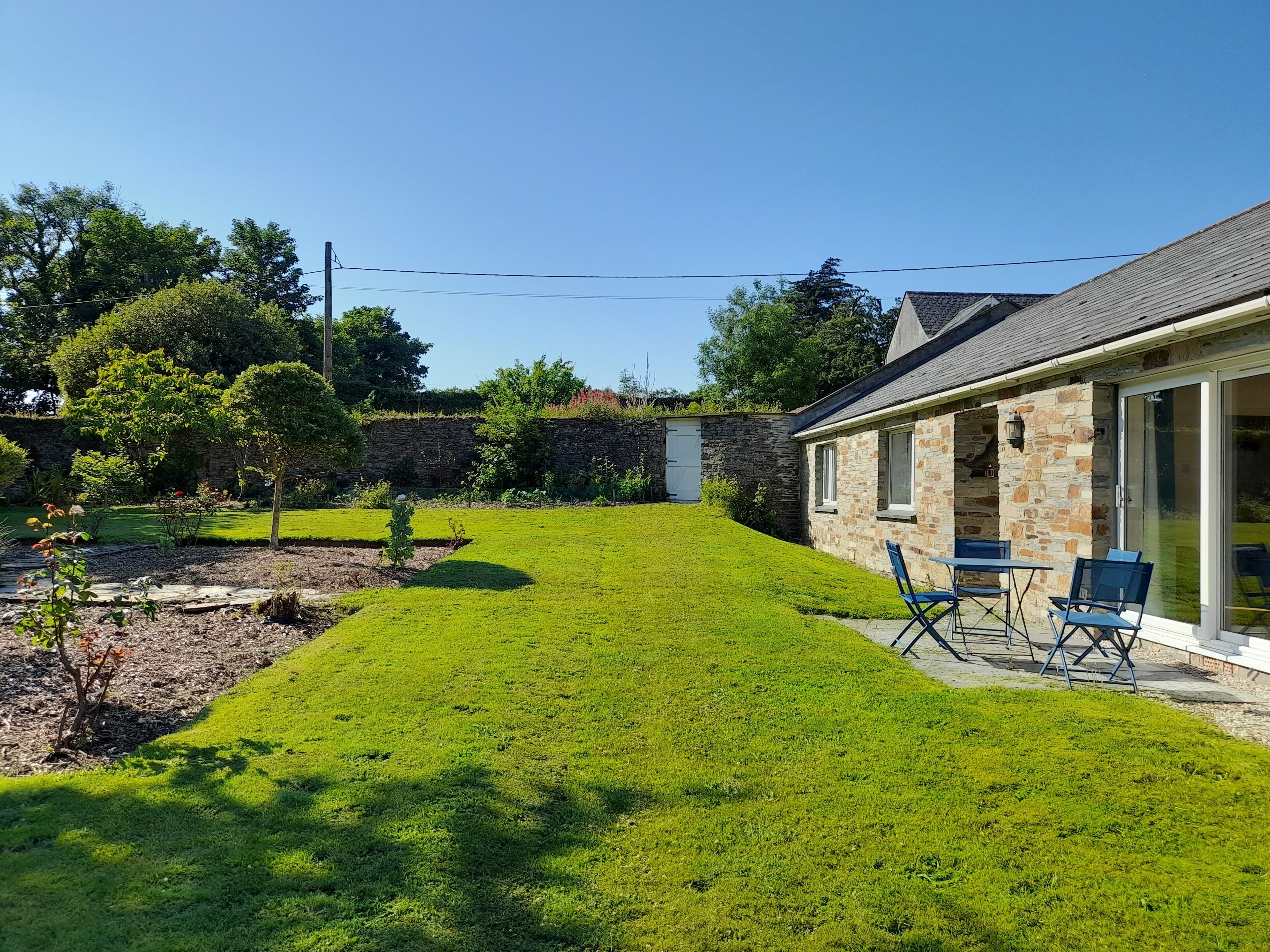 A house with a stone exterior, a grassy backyard, and a patio with chairs.