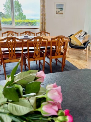 A dining area with a wooden table and chairs, a view of greenery outside, and a framed picture on the wall. - Garden Lodge: your perfect base for exploring Cornwall (Bodmin)