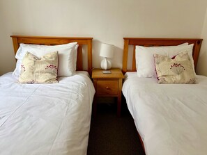 Two single beds with wooden headboards, white bedding, and decorative pillows. - Garden Lodge: your perfect base for exploring Cornwall (Bodmin)