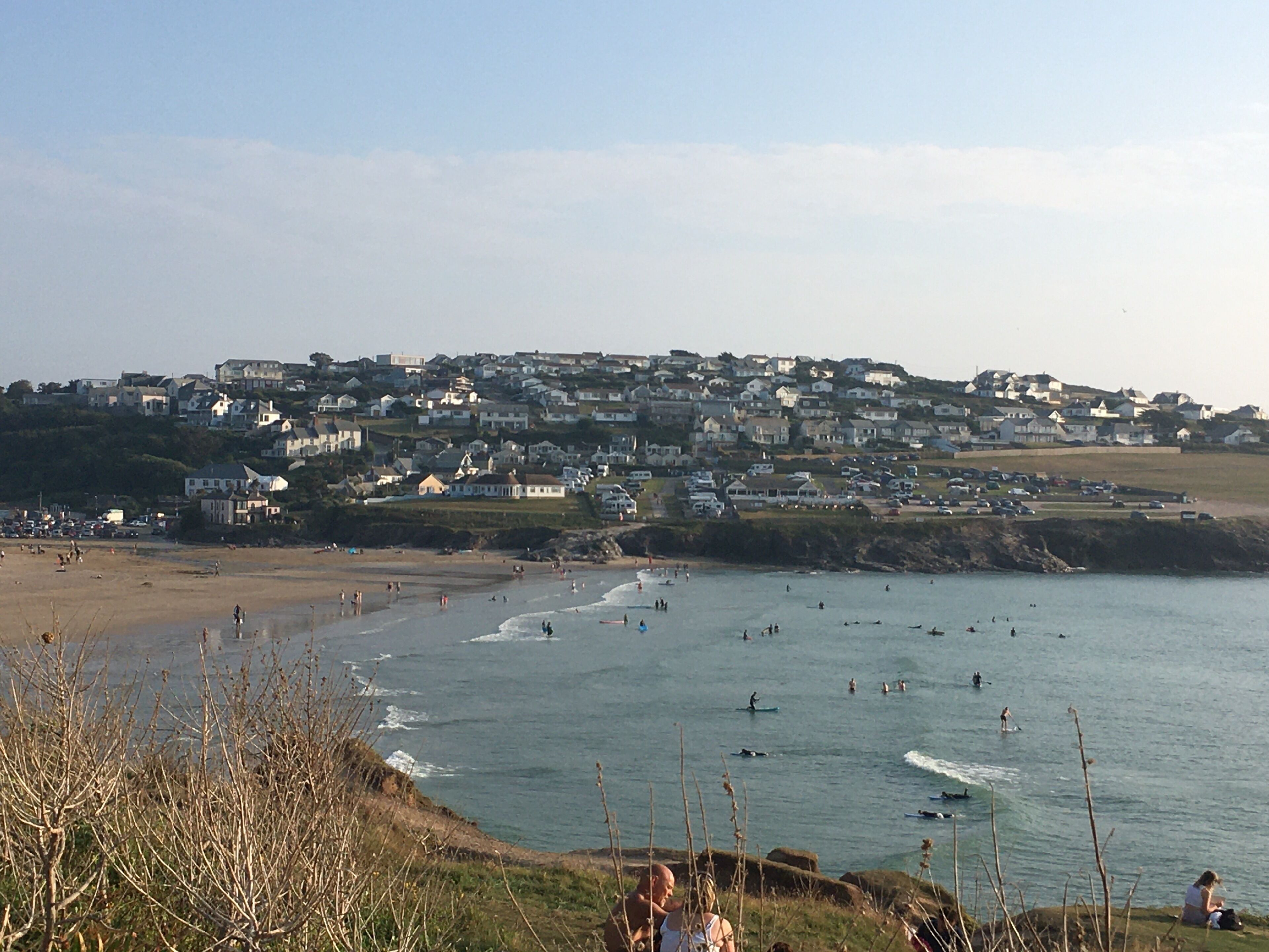 A coastal town with houses along the beach, people surfing, and a clear sky.