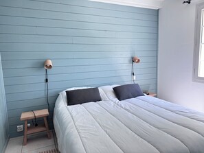 A bedroom with a bed, two bedside lamps, a nightstand, and a window. - Vrbo Property (Saint-Pierre-d'Oléron)
