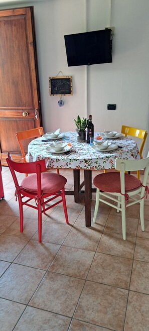 Uma sala de jantar com uma mesa posta para dois, cadeiras, uma televisão presa à parede e uma porta.