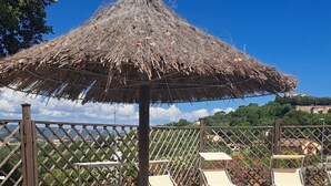 En terrasse med liggestole og en stråparasol, med udsigt over et naturskønt landskab.