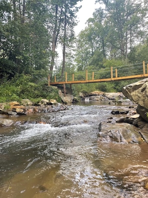 A wooden bridge over a flowing stream with surrounding greenery.