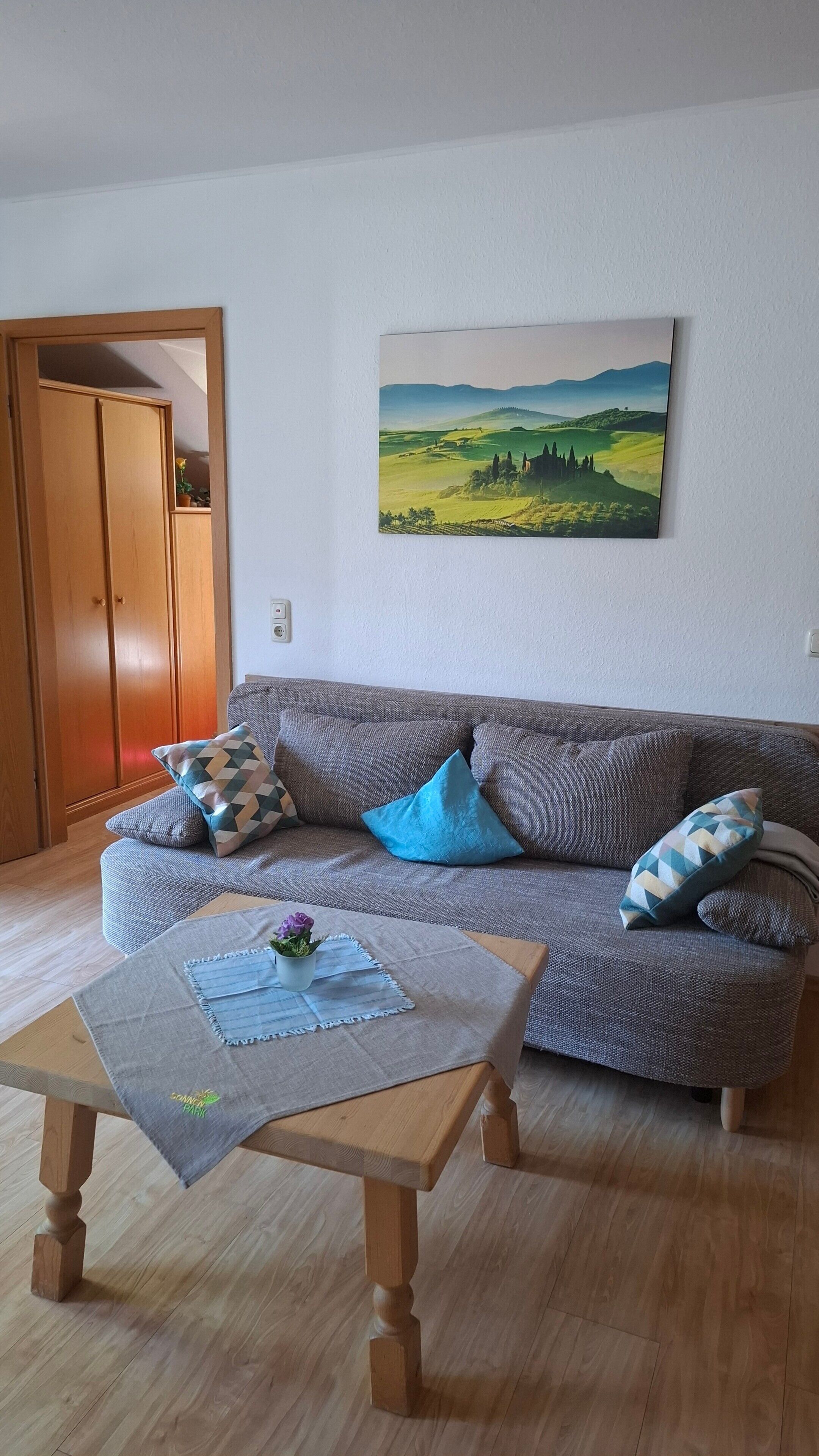 A living room with a sofa, cushions, a coffee table, and a painting on the wall.