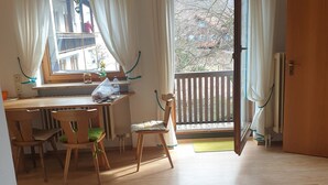 Una habitación con una mesa de madera, una silla, un ventanal con cortinas, un balcón y vistas a edificios.